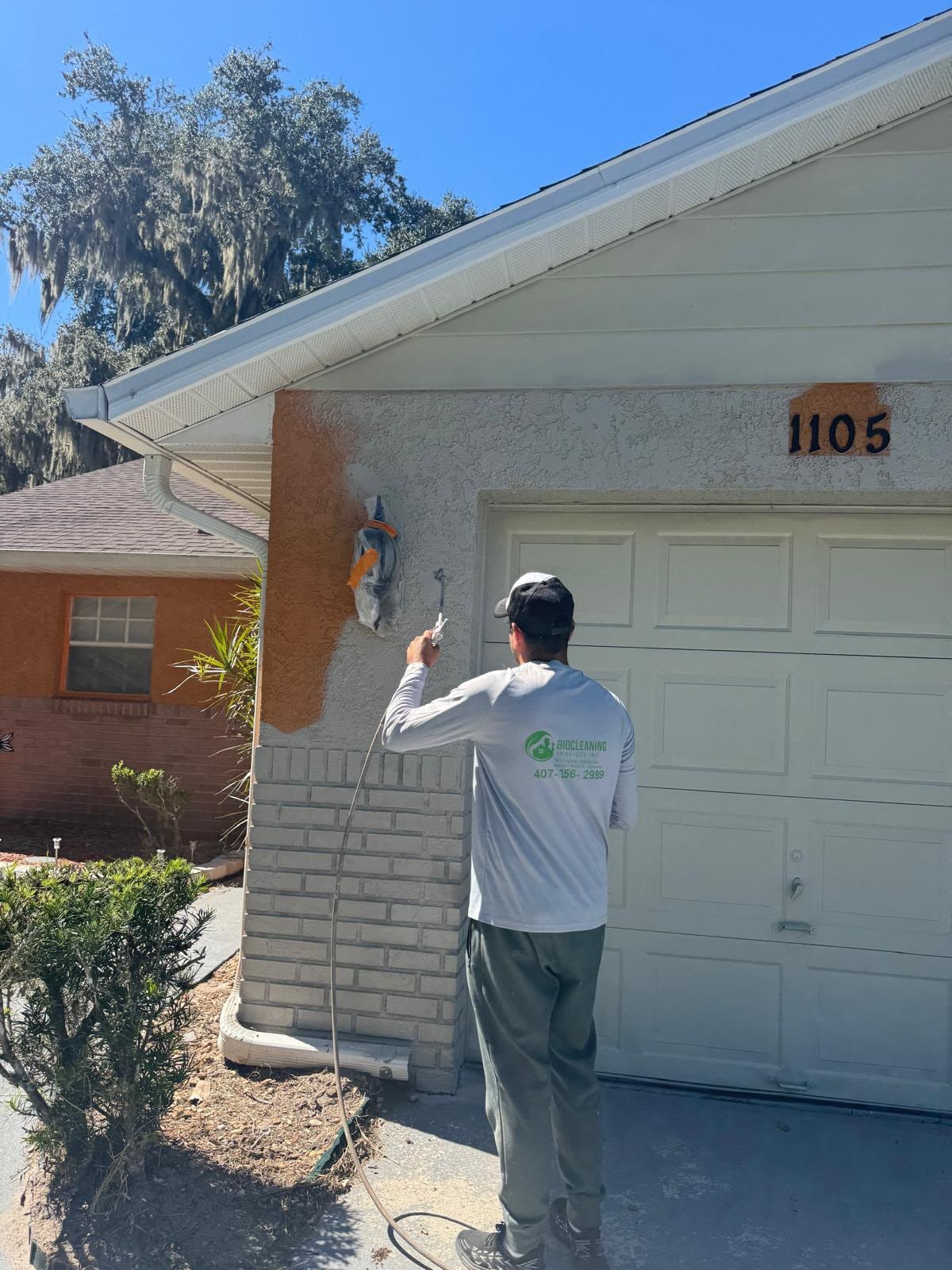 Bio-Cleaning Services technician spray-painting residential exterior — Central Florida.