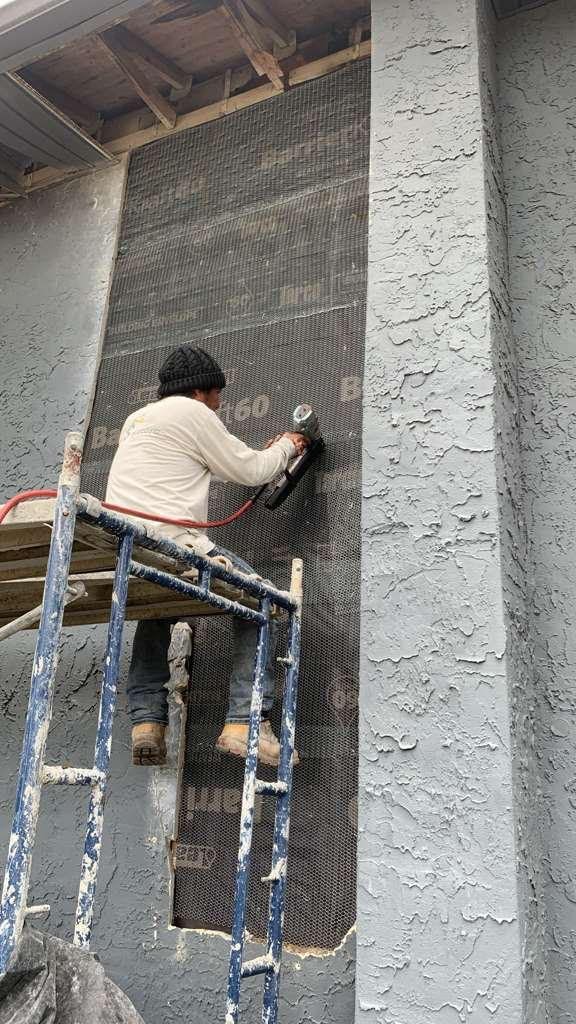 Bio-Cleaning Services technician on scaffolding performing stucco mesh repair on exterior wall — Central Florida.