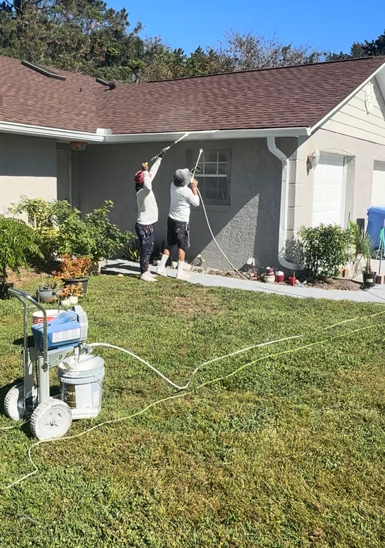 Bio-Cleaning Services crew performing professional exterior painting with spray equipment.